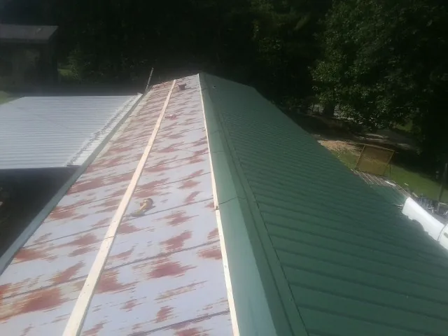 Old rusted panels beside newly installed green metal roofing — Wind Damage Roof Repair by Roofing Brothers in Goshen